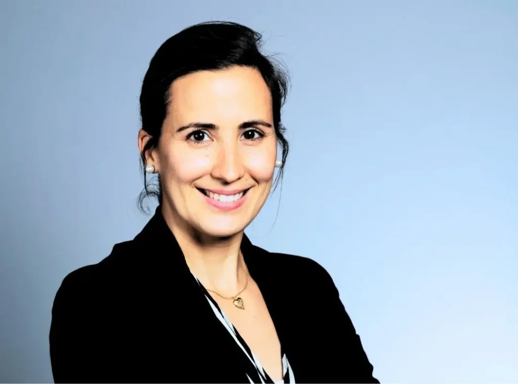 Professional portrait of Andreia Fernandes, smiling and dressed in a black blazer with a heart-shaped necklace, set against a light blue background. Andreia is a career coach and portfolio career facilitator, known for her work in leadership development, failure culture, and purpose-driven career design.